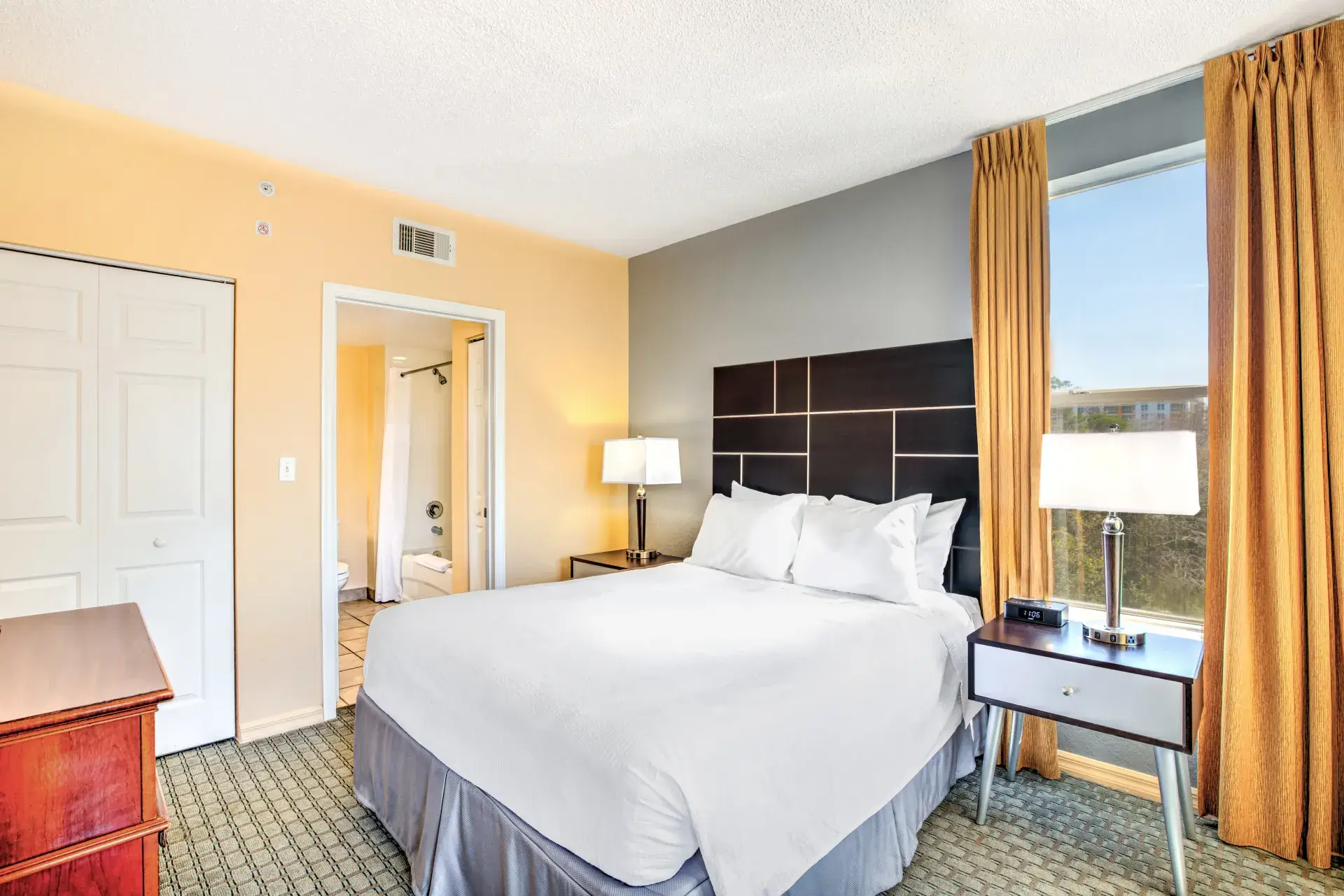 Queen One Bedroom Suite bedroom with a queen bed, dark headboard, nightstands with lamps, and a window overlooking the resort
