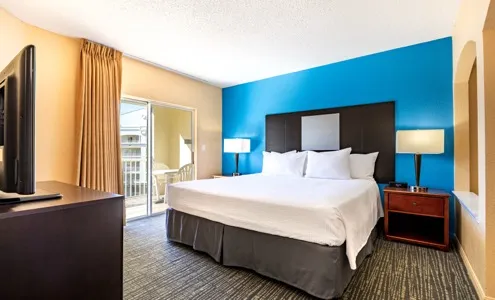 King bedroom with blue accent wall, dark upholstered headboard, and balcony door